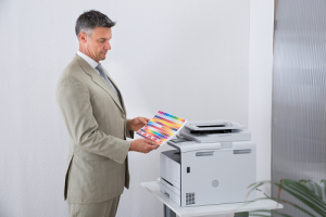 Businessman holding a sheet of colored paper material while stranding in front of copier machine