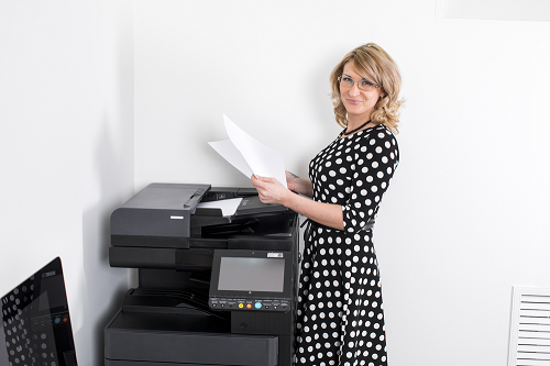 woman wearing polka dot dress standing infront a copier machine while while sheets of paper