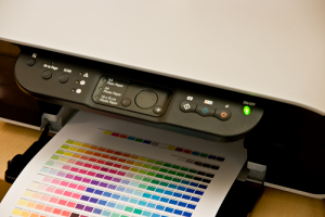 Black and white printer showing green power light and a white sheet of printed color coded paper inserted in tray