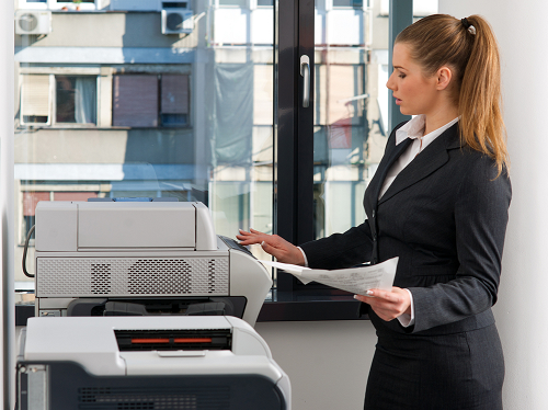 Young female business woman holding papers in hand while standing in front copier machine