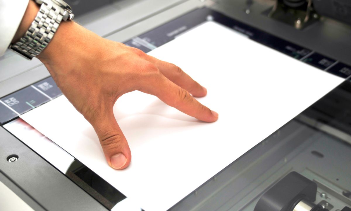 a person's hand pressing a piece of paper into a copier